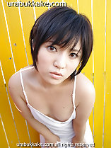 Standing in front of yellow fence short hair wearing white slip leaning forward